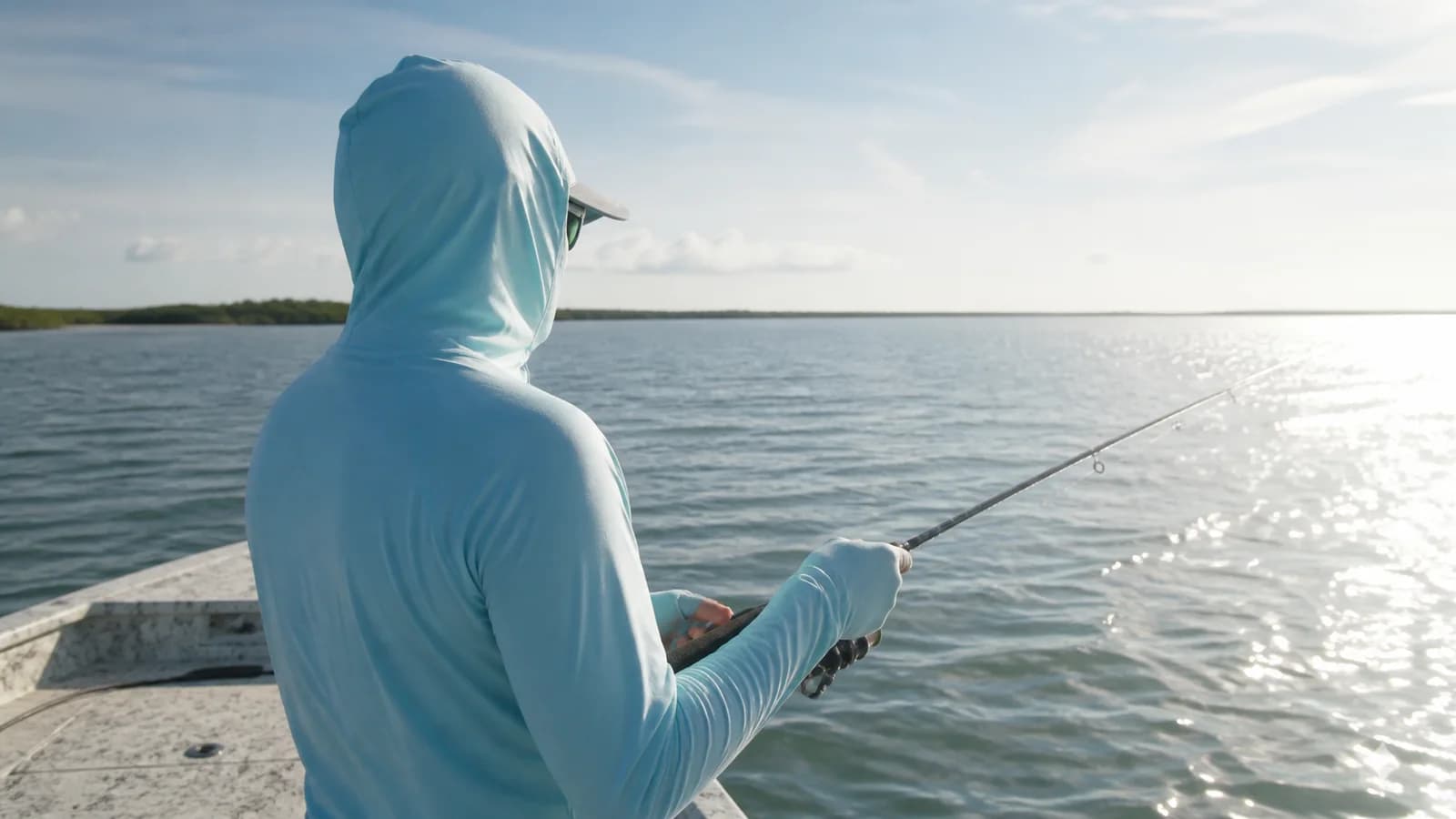 Angler wearing a generic pale blue sun hoodie while fishing from a small boat