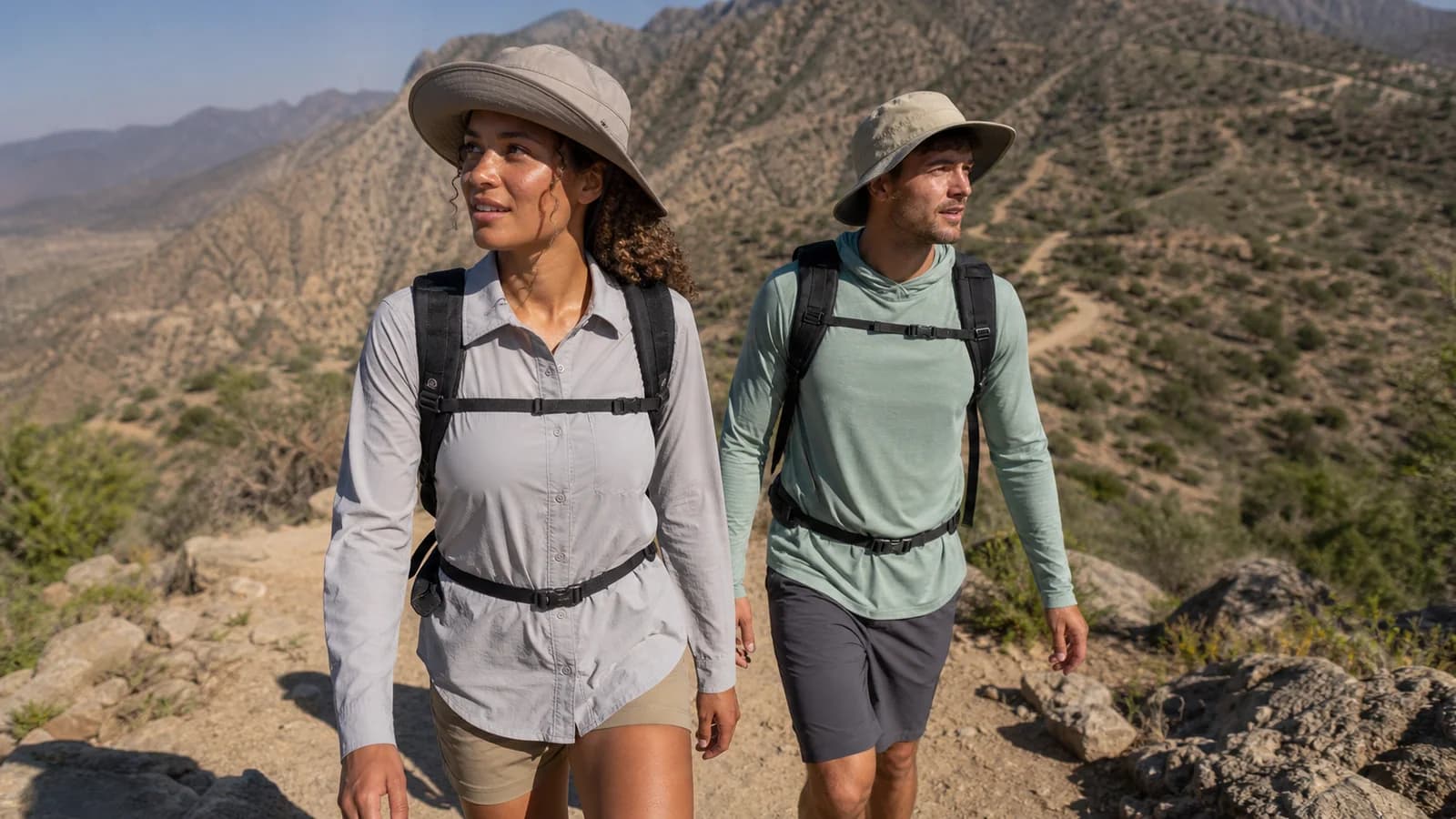 Two hikers in lightweight long-sleeve shirts pausing on a hot open trail